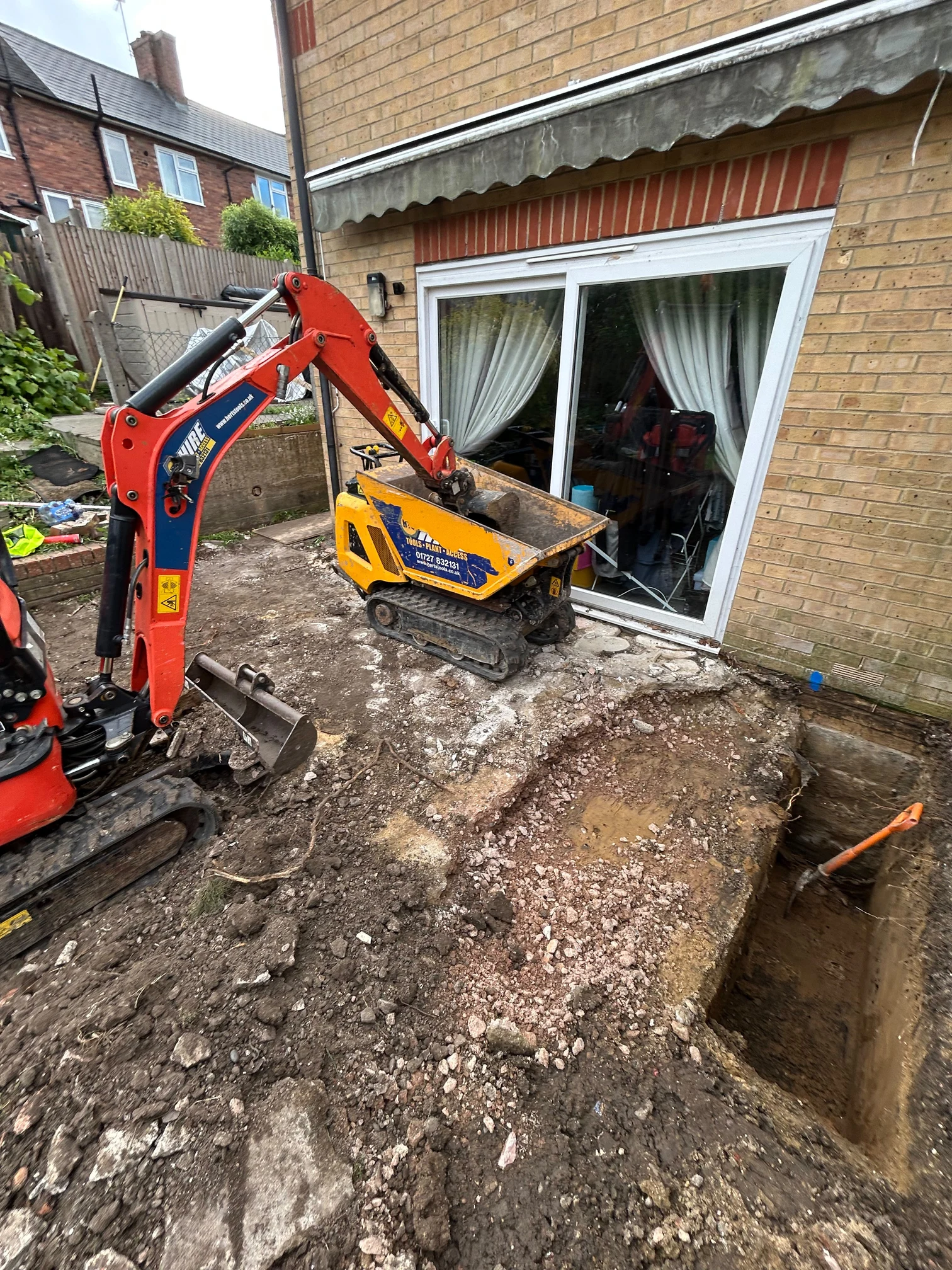 Before: rear of the house with the original patio doors, a mini excavator, a tracked dumper and excavation in the garden