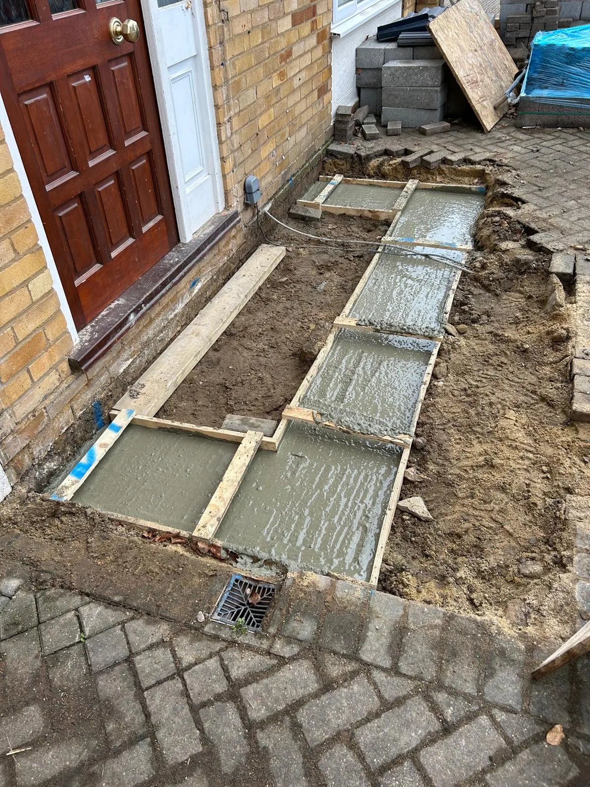 Freshly poured concrete strip footings shuttered in timber beside a front door