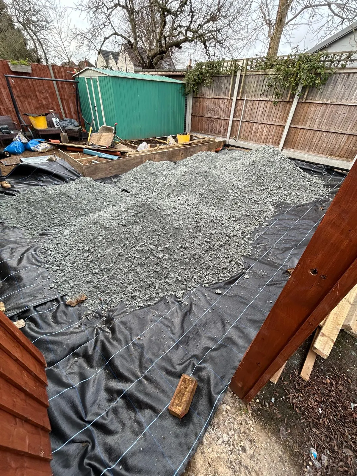 Piles of crushed sub-base aggregate tipped on a geotextile membrane in a rear garden