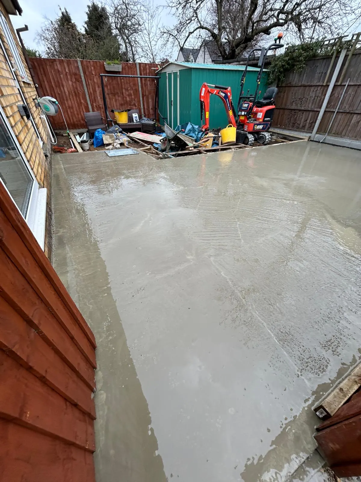 Freshly poured and levelled concrete slab across the full width of a rear garden